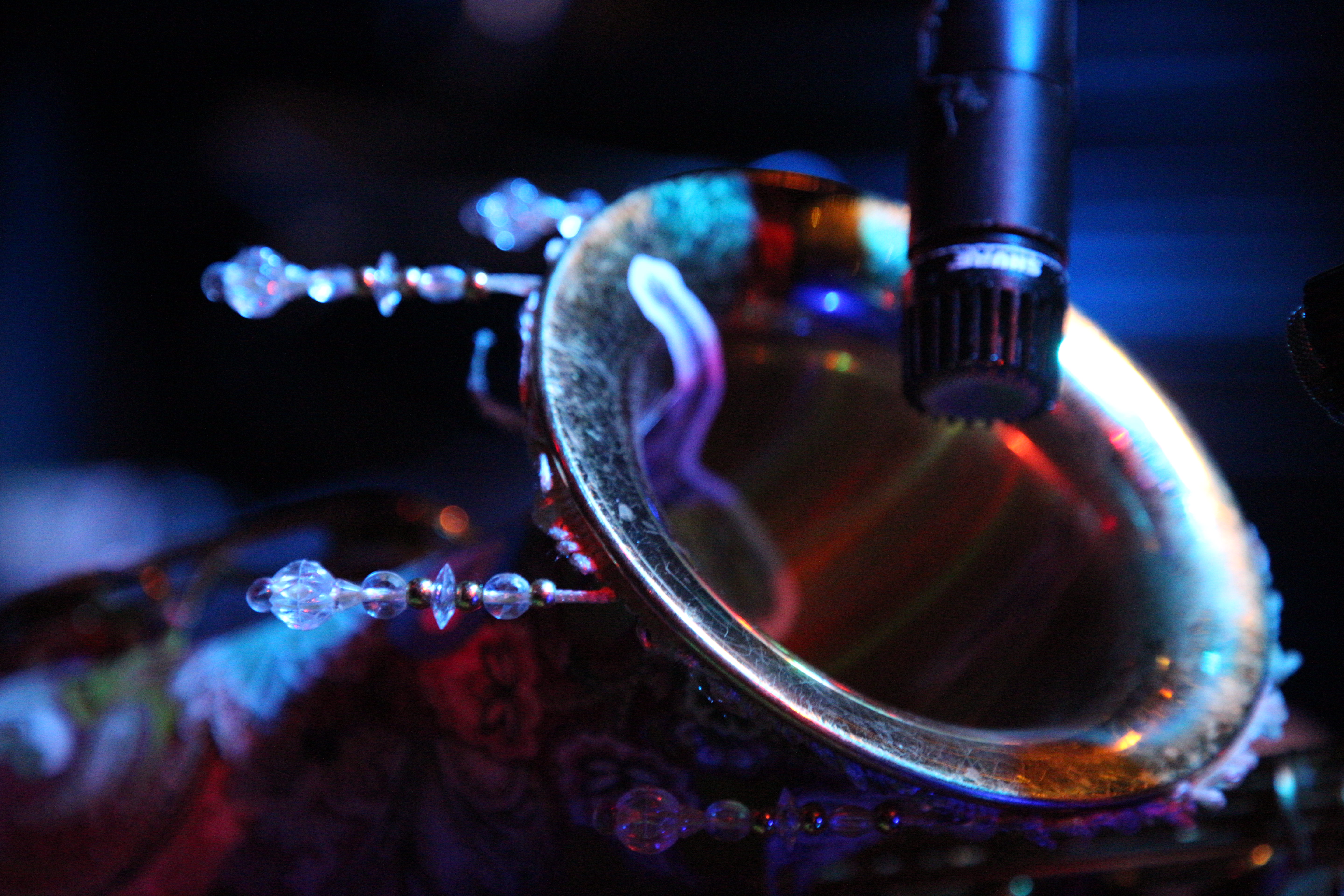 Close-up of a mic'd brass horn bell trimmed with crystal beads under blue stage light