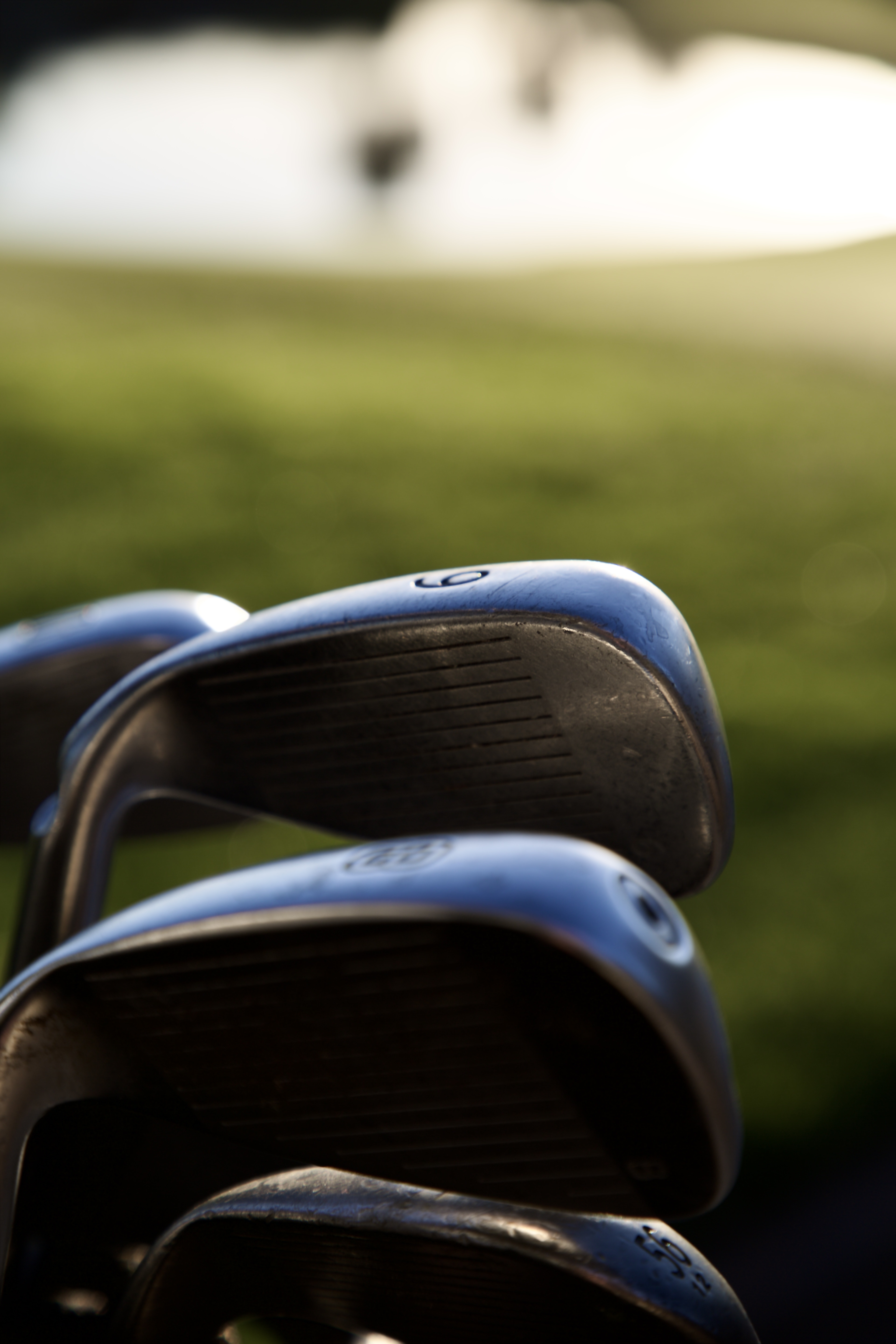 Close-up of blue-topped golf irons racked together with the course softly blurred behind