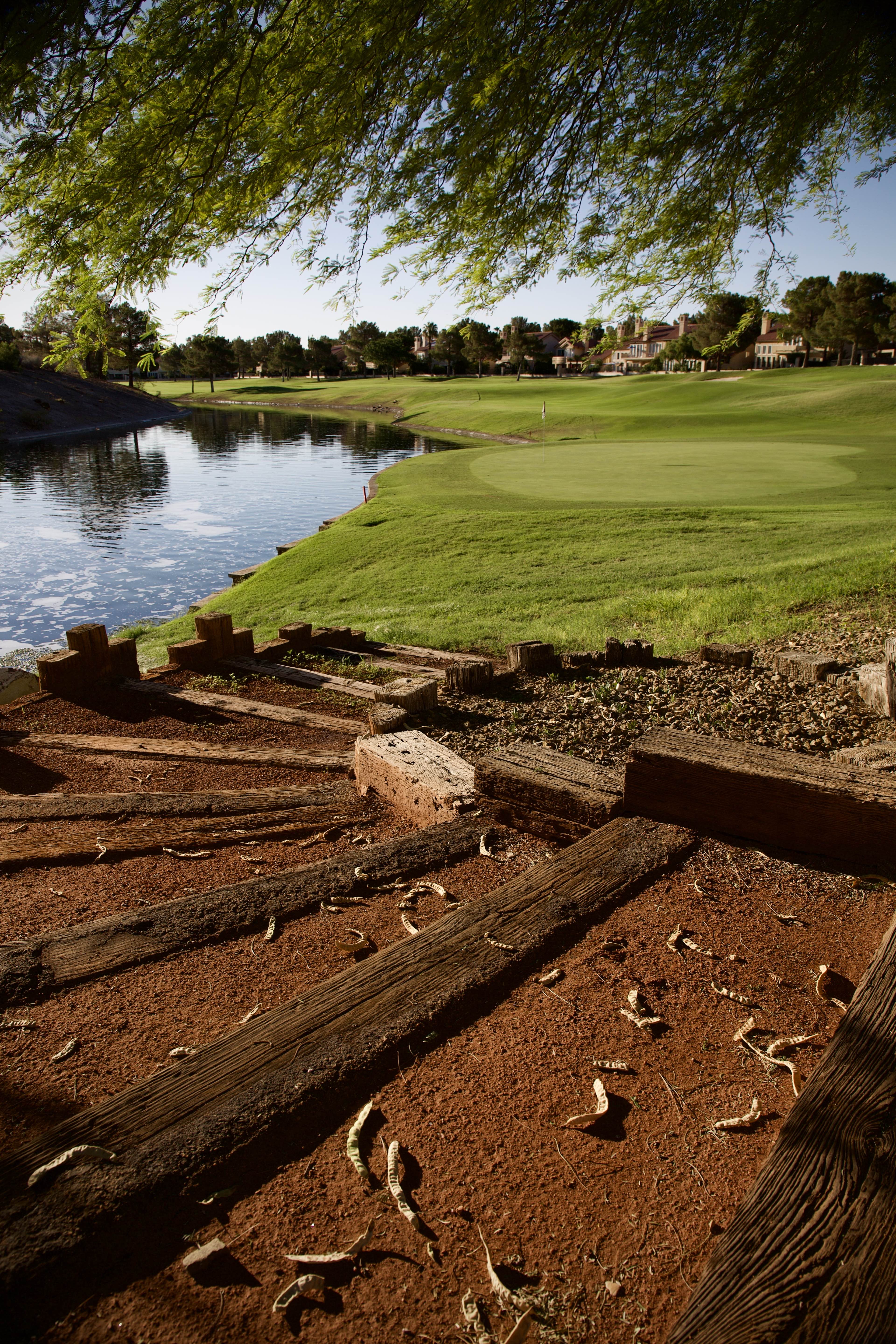 Weathered railroad-tie steps on red desert soil leading down to a pond with a flagged green beyond