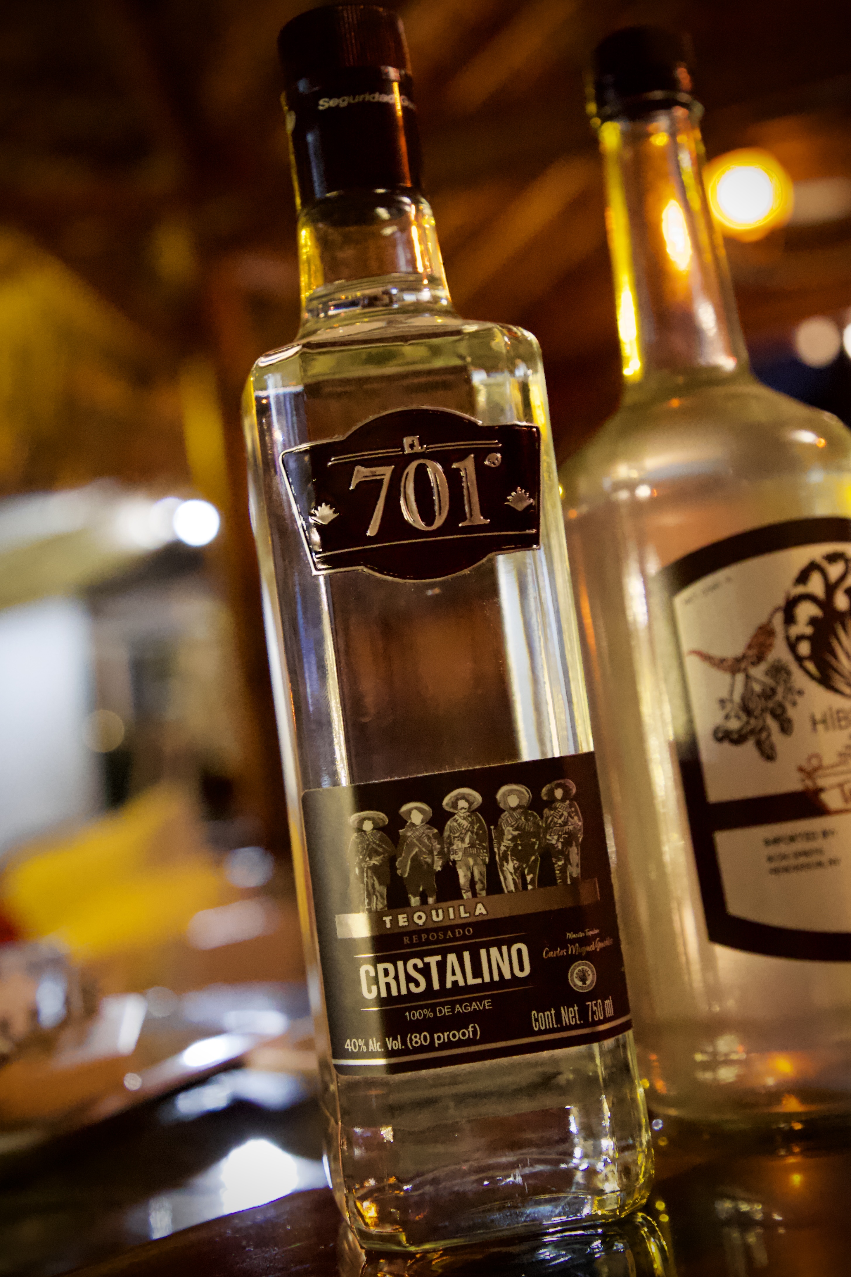 701 Cristalino Reposado bottle lit to show the revolucionario figures label in a warm bar