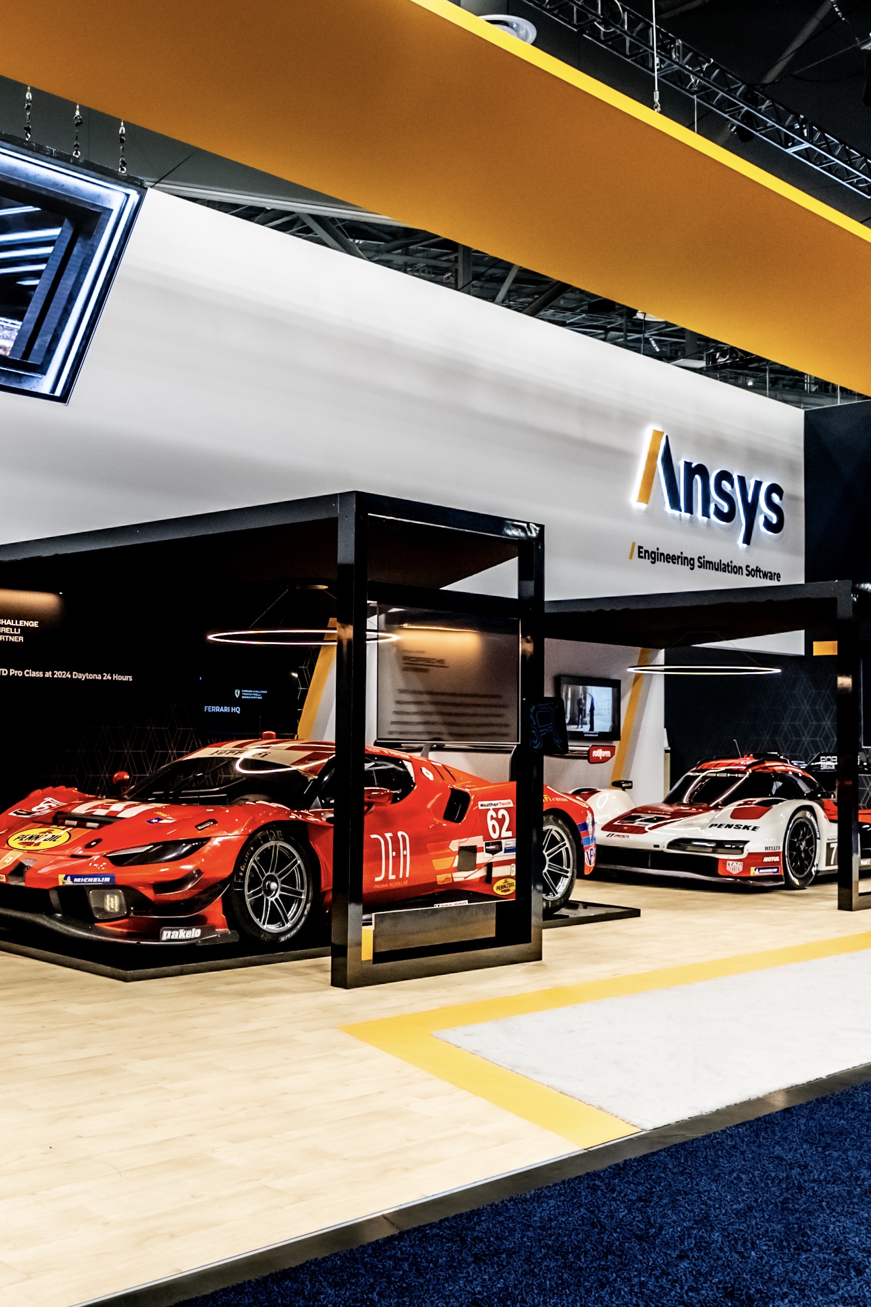 Ansys engineering-simulation exhibit with a Ferrari and Porsche race car displayed under an illuminated sign